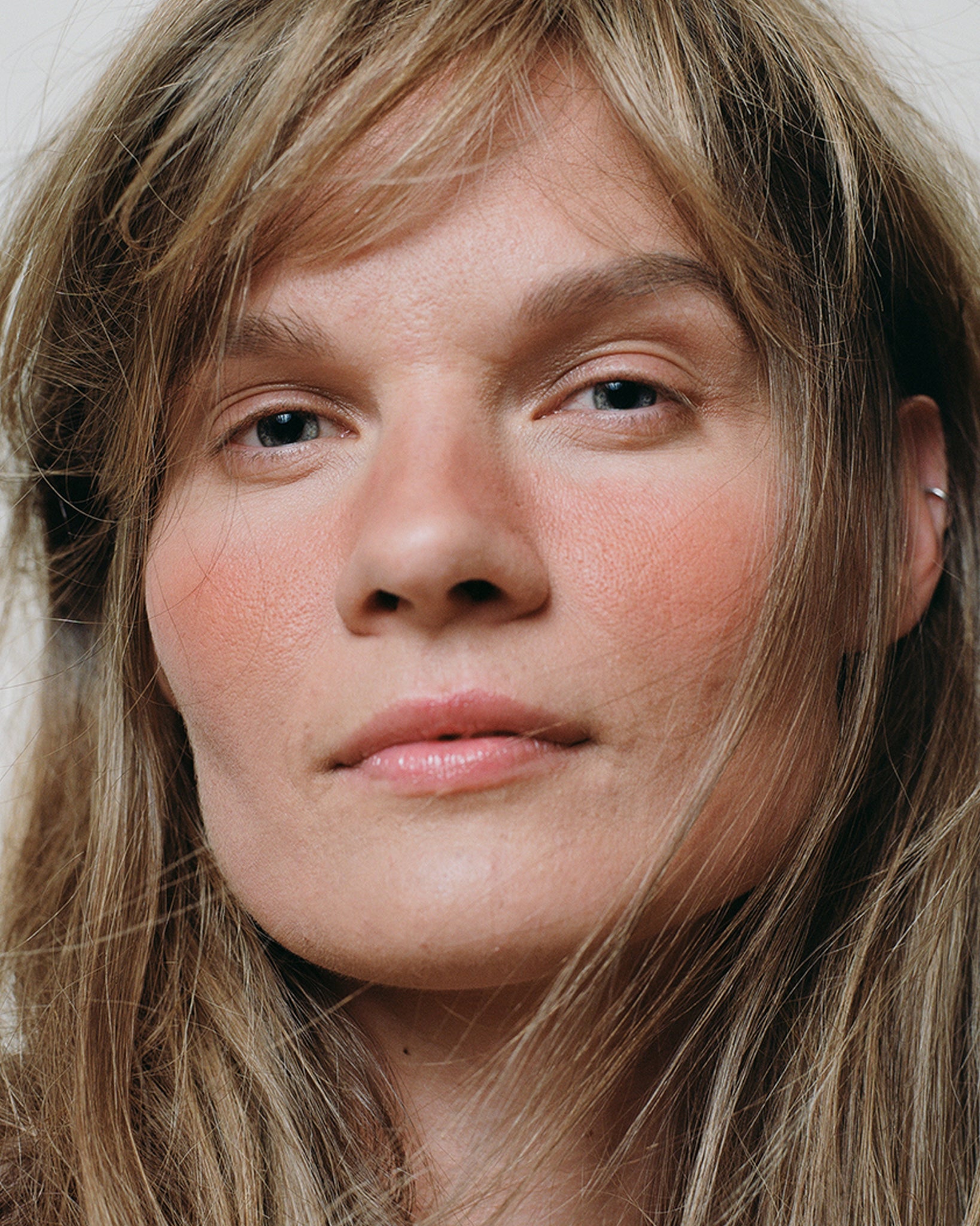 Model wearing MÁDARA Organic Skincare mineral cheek blush fierce flame on A6821 on skin; close-up portrait shows natural application results.