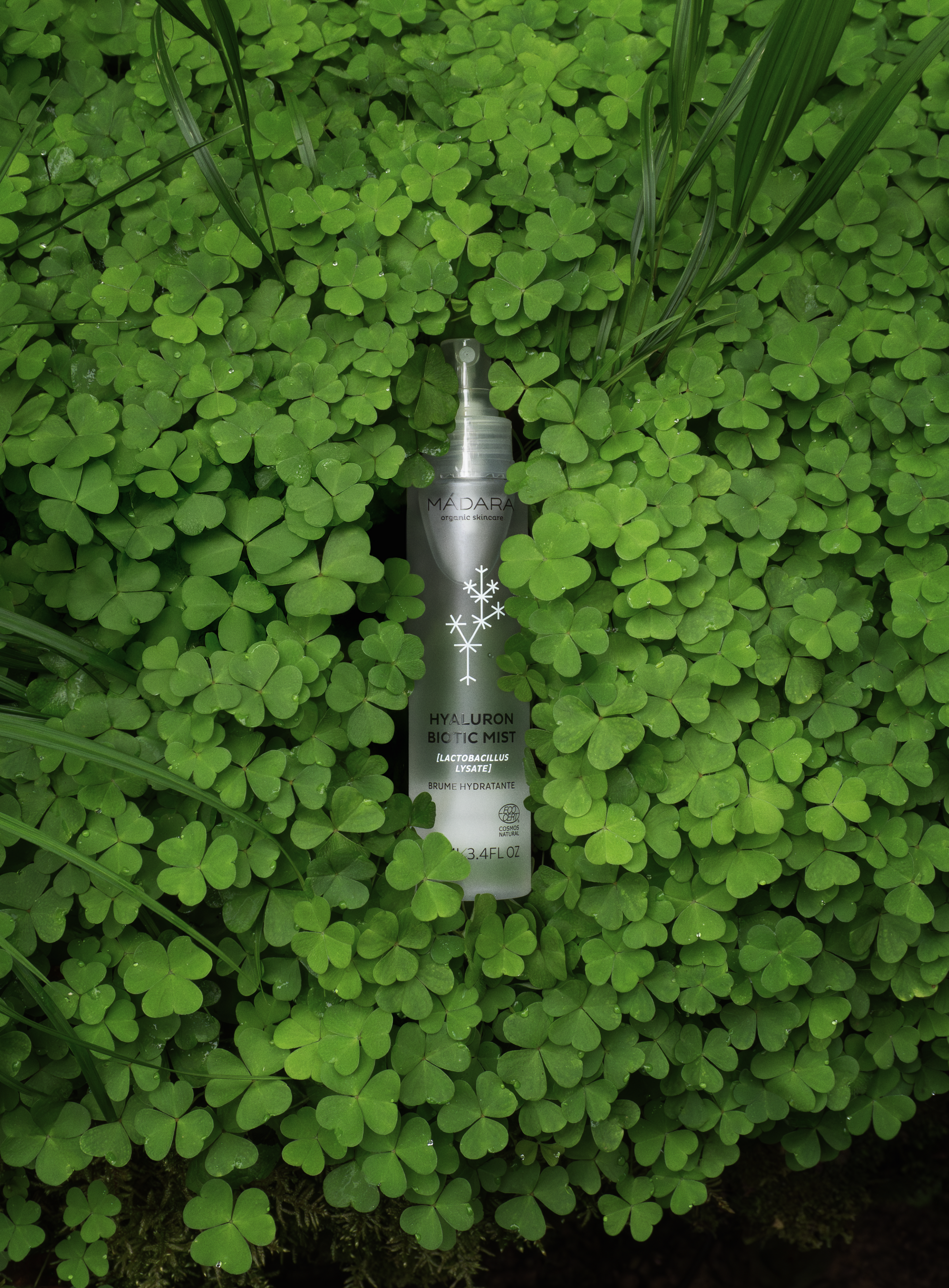MÁDARA Hyaluron Biotic Mist bottle placed in fresh green clover leaves, symbolizing natural and organic skincare ingredients